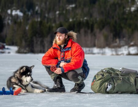 A man and his husky enjoy a winter ice fishing trip on a frozen lake.